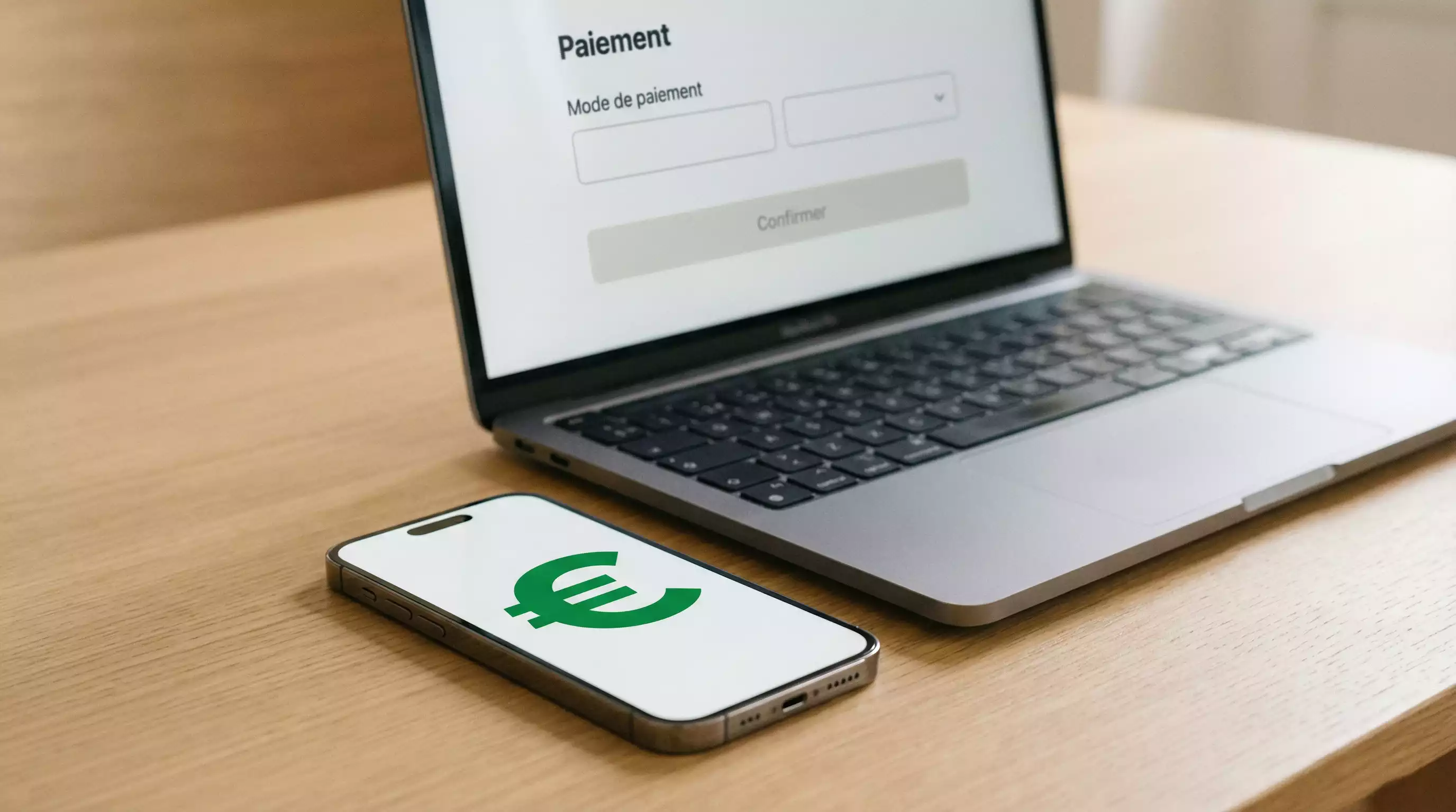 Smartphone posé sur une table avec un symbole € affiché à l'écran à côté d'un ordinateur portable ouvert