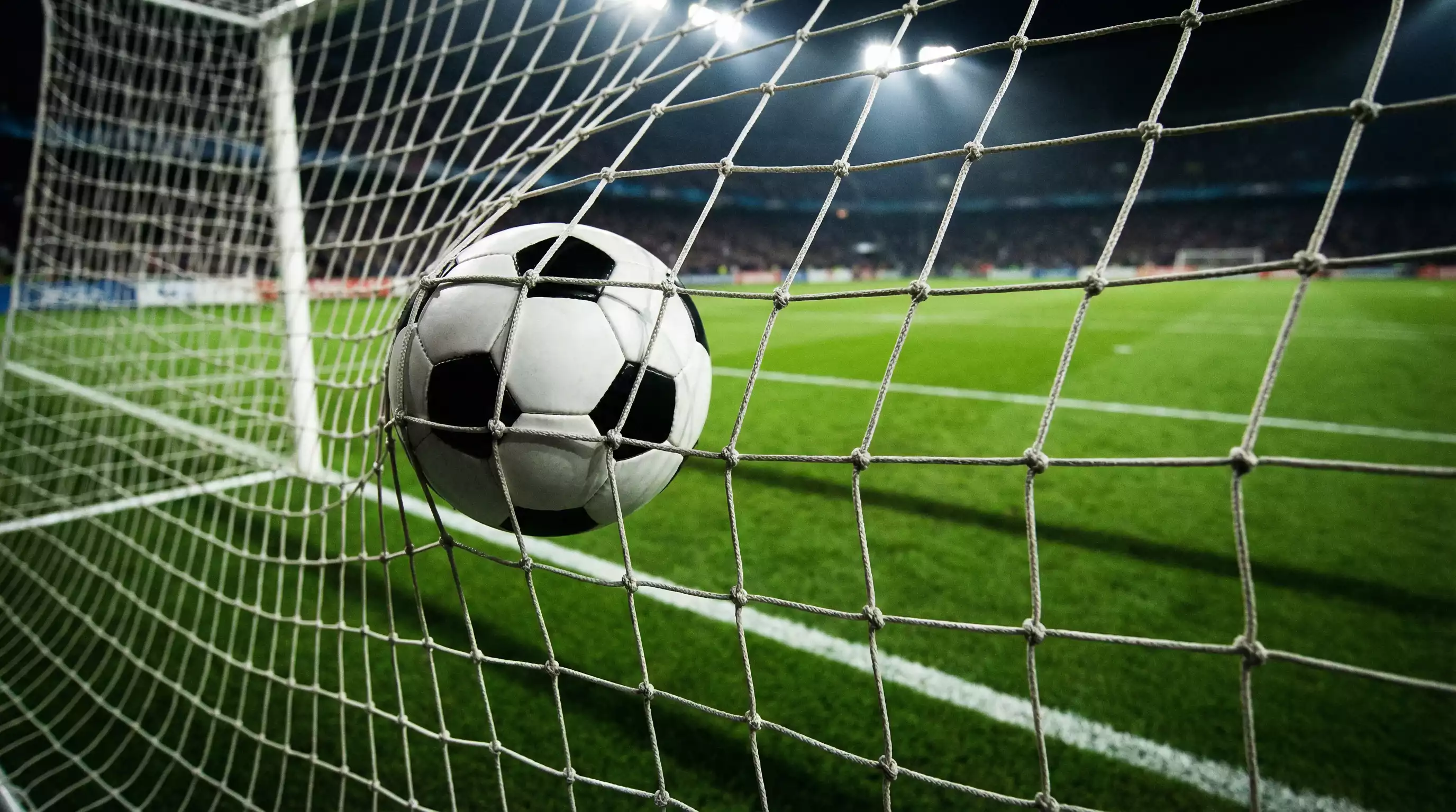 Filet de but de football vu de l'intérieur avec un ballon franchissant la ligne dans un stade éclairé